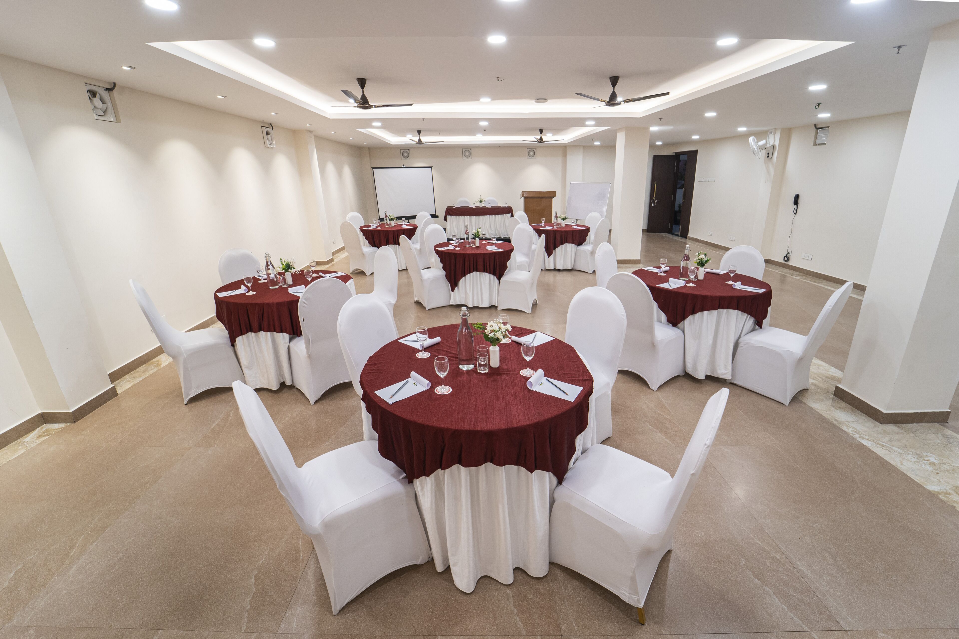 Un salón de conferencias con varias mesas redondas, sillas blancas y manteles rojos.
