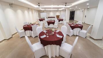 Un salón de conferencias con varias mesas redondas, sillas blancas y manteles rojos.