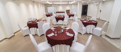 Un salón de conferencias con varias mesas redondas, sillas blancas y manteles rojos.