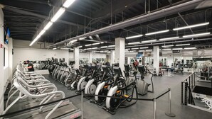 Un gimnasio con numerosas cintas de correr alineadas, diversas máquinas de ejercicio y un espacio amplio.