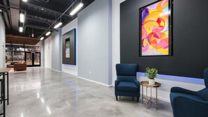 Un vestíbulo amplio con diseño moderno, que incluye un sillón azul, una pequeña mesa redonda con una planta y un cuadro abstracto grande en la pared.