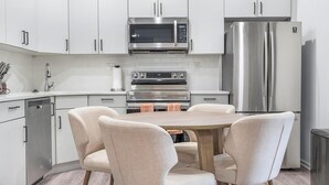 Una cocina moderna con armarios blancos, electrodomésticos de acero inoxidable y una mesa redonda con cuatro sillas.