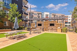 A courtyard with picnic tables, a barbecue area, and a pergola with string lights.