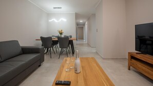 A modern living room with a sofa, a wooden coffee table with a remote control, a dining table with chairs, and a TV on a wooden stand. - Lovely apartment in Mrljane (Mrljane)