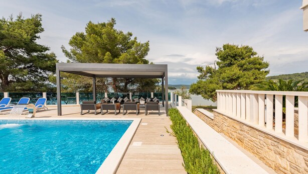 A poolside area with a covered seating area, lounge chairs, and a view of the sea. - Lovely apartment in Mrljane (Mrljane)