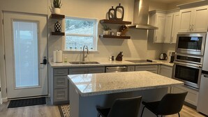 Cocina moderna con una isla grande, electrodomésticos de acero inoxidable y ventana con vistas a árboles.
