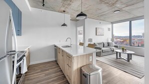 Une cuisine moderne dotée d’un grand îlot central, d’un coin repas avec un canapé et une petite table, et offrant une vue sur la ville grâce à de grandes fenêtres.