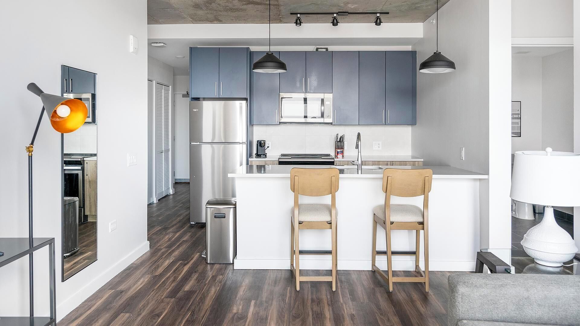 Une cuisine moderne avec des meubles gris, un réfrigérateur en acier inoxydable et un îlot central doté de deux tabourets de bar.