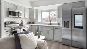 Une cuisine moderne dotée d’appareils électroménagers en acier inoxydable, de meubles de rangement gris et d’une fenêtre offrant une vue sur l’extérieur.