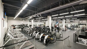 Une salle de sport équipée de plusieurs tapis de course, d’appareils de musculation et de poids libres.