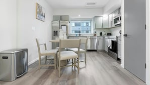 A modern kitchen with white cabinets, a stainless steel refrigerator, and a dining area with light-colored chairs. - Landing | Stunning 2BD, Clubhouse, Gym (Philadelphia)