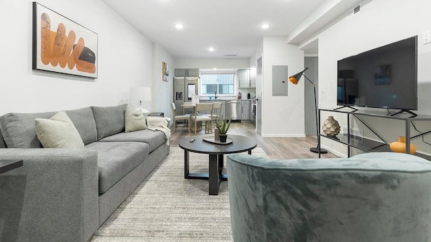 A modern living room with a grey sofa, a round coffee table, and a TV on a stand. - Landing | Stunning 2BD, Clubhouse, Gym (Philadelphia)