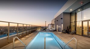 A rooftop pool with a city view, lounge chairs, and a glass railing.