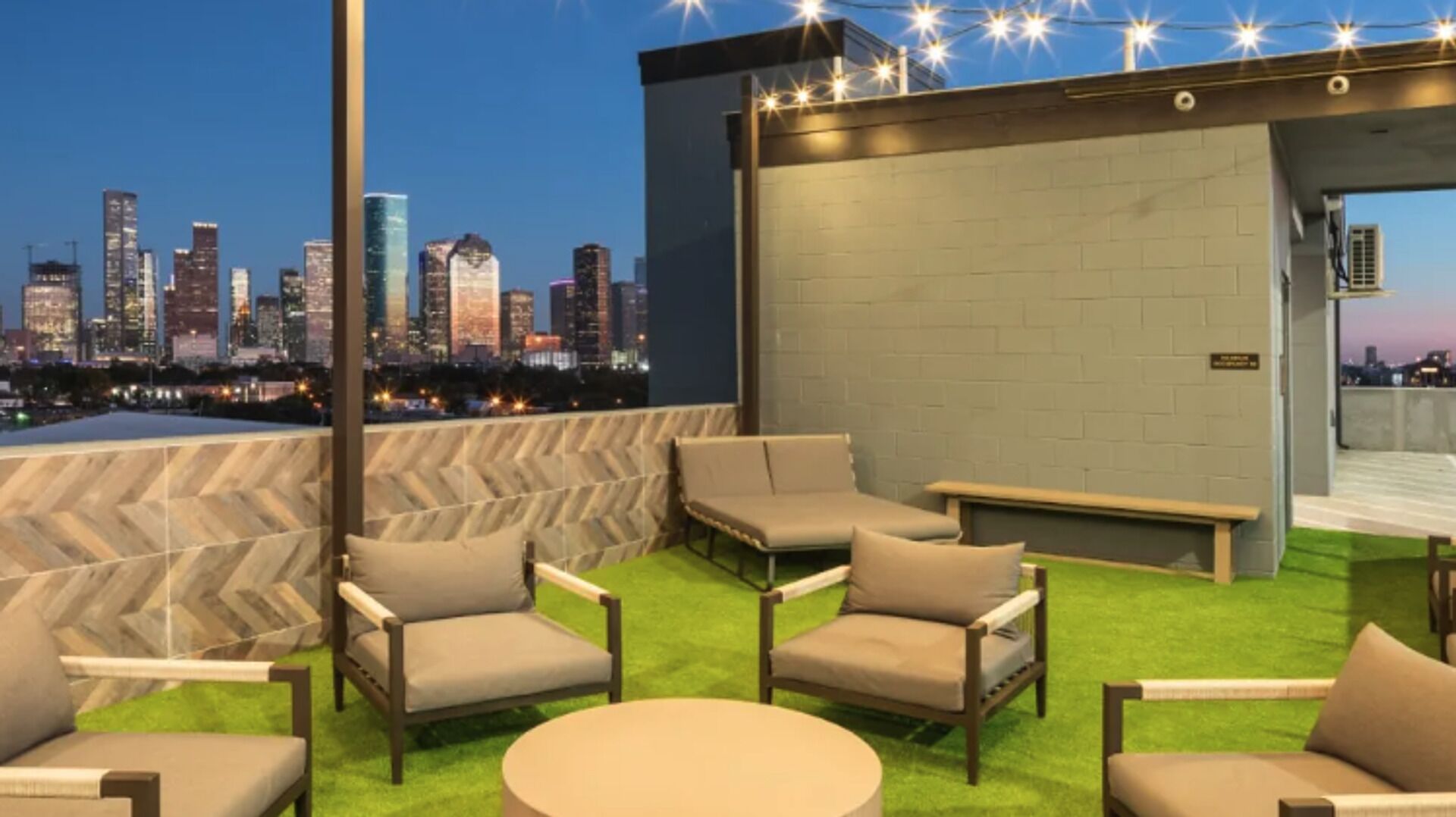 A rooftop terrace with outdoor seating, a view of a city skyline, and a modern building structure.