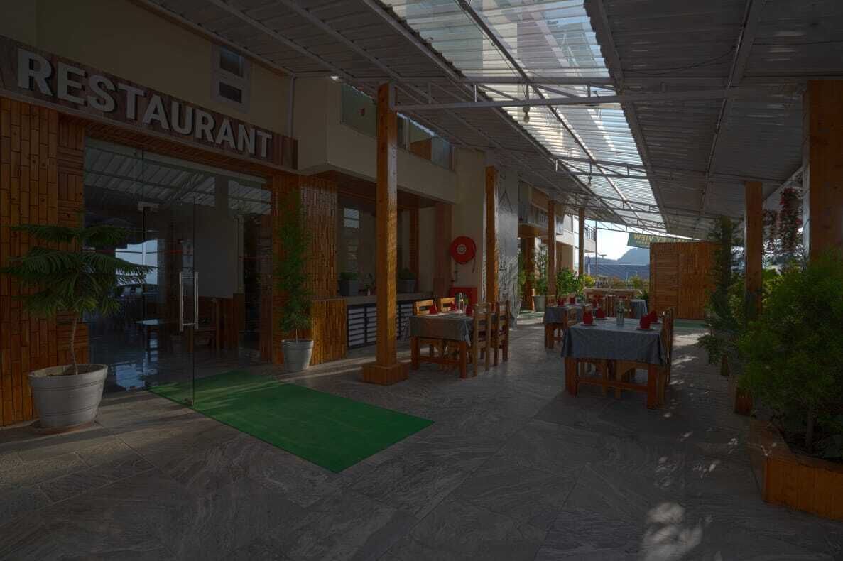 Un restaurante con terraza cubierta, pilares de madera y plantas en macetas.