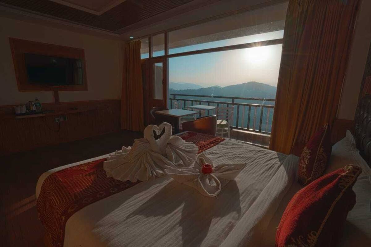 A hotel room with a large bed, a TV, a balcony with a mountain view, and a small table.