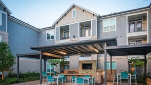 Un immeuble résidentiel à plusieurs étages doté d’un patio extérieur couvert, comprenant un barbecue et des sièges.