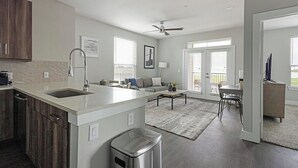 Une cuisine moderne avec un îlot central, un coin repas avec une table et des chaises, un salon avec un canapé et un téléviseur placé dans un coin.