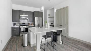 A modern kitchen with grey cabinets, stainless steel appliances, a white island with bar stools, and a grey door.