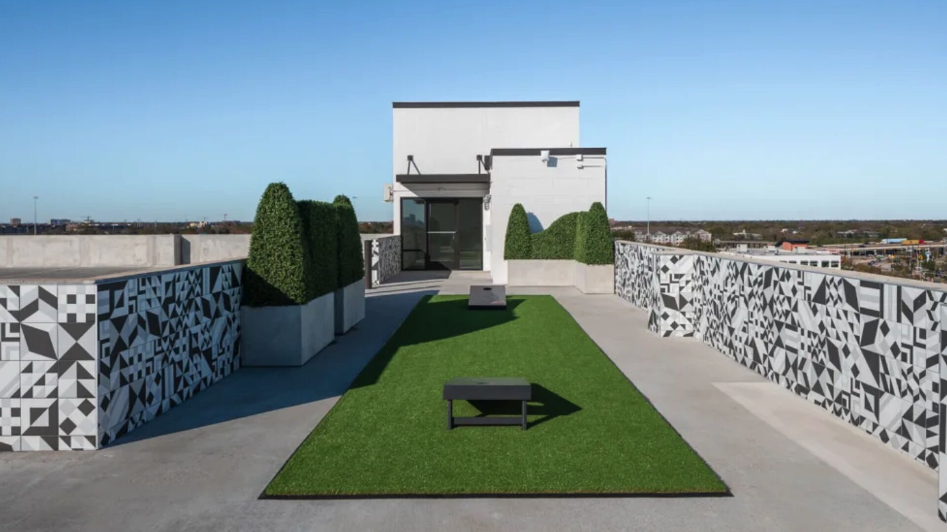 A rooftop terrace with a geometric patterned wall, a small table, and neatly trimmed bushes.