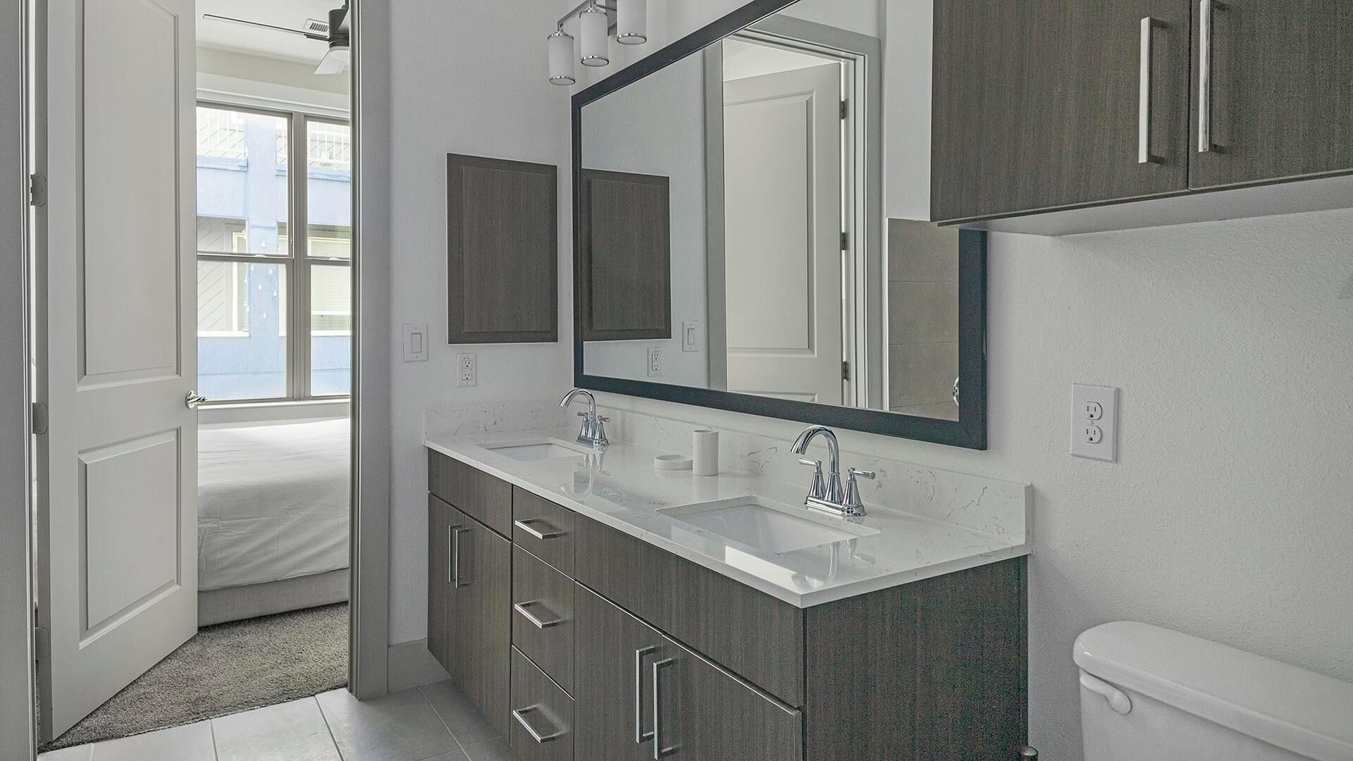 A modern bathroom with a double sink, a large mirror, and a toilet.