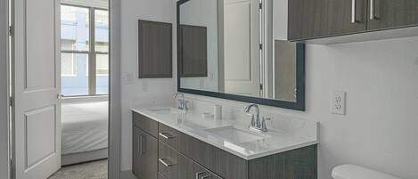 A modern bathroom with a double sink, a large mirror, and a toilet.