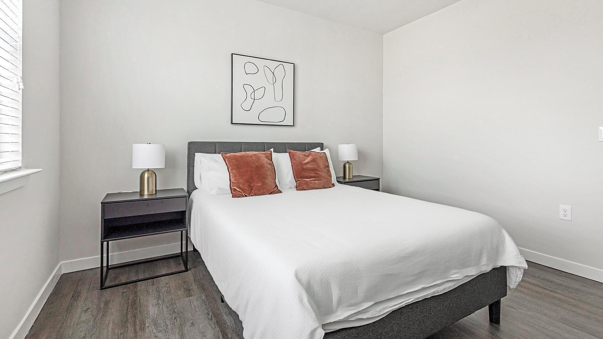 Una camera da letto moderna con un letto grande, due comodini con lampade e un'opera d'arte astratta appesa al muro.