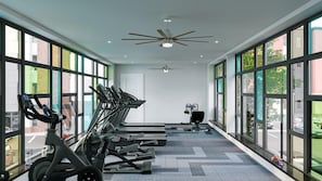 Ein Fitnessraum mit Laufbändern, einem Deckenventilator und großen Fenstern.