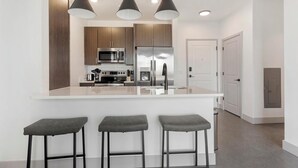 A modern kitchen with a central island, stainless steel appliances, and bar stools. - Landing | Amazing 2BD, Clubhouse, Gym (Richmond)