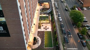 Vista aérea de um edifício moderno com um jardim no terraço, um caminho curvo e um estacionamento.