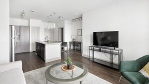 A modern living room with a flat-screen TV, a green armchair, and a round coffee table with a plant.