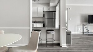 Uma cozinha moderna com eletrodomésticos de aço inoxidável, um banquinho de bar e uma área de jantar com uma mesa redonda e cadeiras.