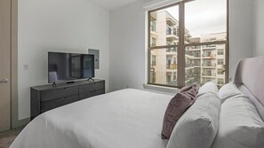 Une chambre avec un grand lit, un téléviseur posé sur une commode et une fenêtre donnant sur la ville.