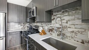 Une cuisine moderne avec des meubles en bois foncé, des appareils en acier inoxydable, un plan de travail en marbre blanc et un mur de fond en briques vieilli.