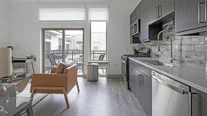 Une cuisine moderne équipée d’appareils électroménagers en acier inoxydable, un coin repas avec un canapé en cuir et un balcon offrant une vue sur la ville.