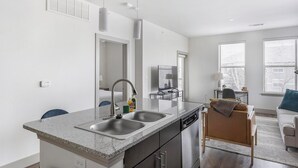 Eine moderne Küche mit Granit Arbeitsplatte, Edelstahlspüle und Geschirrspüler. Es gibt einen Essbereich mit Tisch und Stühlen sowie ein Wohnzimmer mit Sofa und Fernseher.