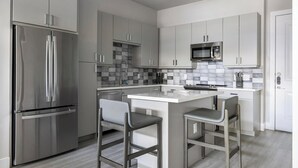 Eine moderne Küche mit grauen Schränken, einem Edelstahl-Kühlschrank, einer Mikrowelle und einer zentralen Kochinsel mit Barhocker.