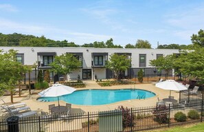 A modern building with a swimming pool, outdoor seating, and a fenced patio area.