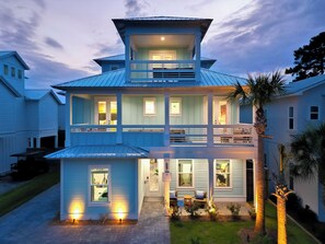 A two-story house with a balcony, a covered porch, and a well-lit entrance. - Sandy Shores | Private Pool | Putting Green | Private Beach Access (Miramar Beach)