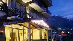 A hotel with a glass facade, outdoor seating, and a mountain backdrop. - The Spruce Mansion Manali (Manali)