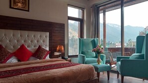 A bedroom with a large bed, a headboard, a nightstand, a lamp, and a window with a mountain view. - The Spruce Mansion Manali (Manali)