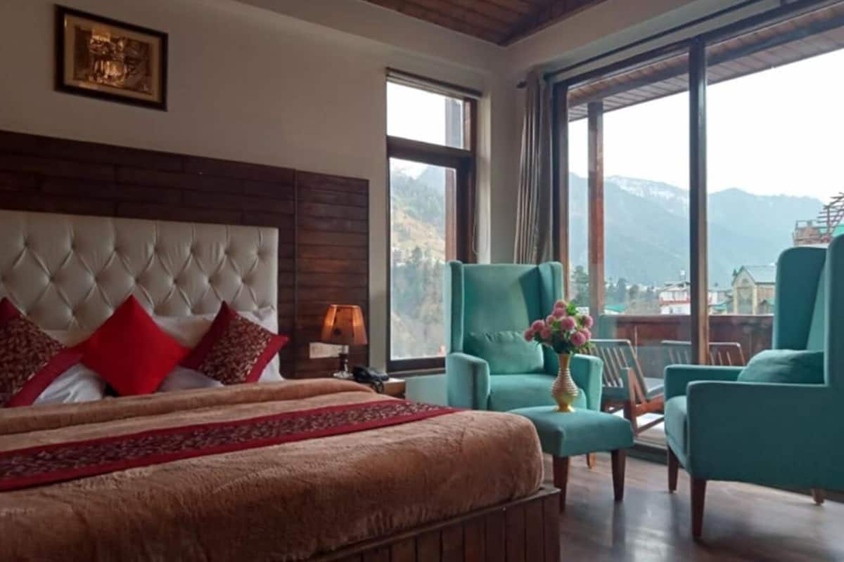 Un dormitorio con una cama grande, cabecera, mesita de noche, lámpara y ventana con vista a la montaña.