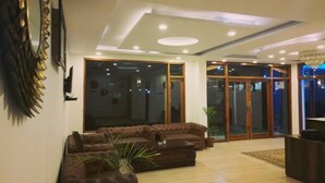 A modern living room with a brown sectional sofa, a coffee table, and a large mirror on the left. There is a sliding glass door leading to an outdoor area. - The Spruce Mansion Manali (Manali)