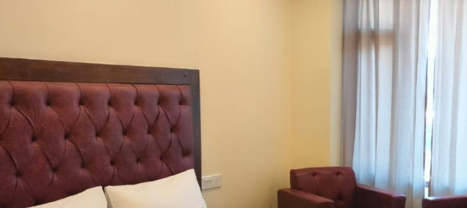 A room with a tufted headboard, a bed with white pillows, and a red armchair.