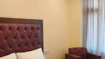 A room with a tufted headboard, a bed with white pillows, and a red armchair.