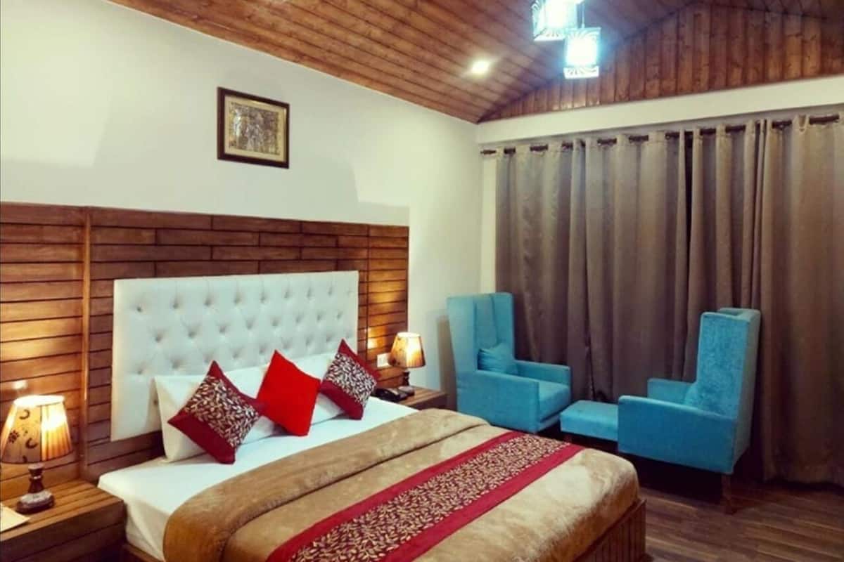 Habitación de hotel con una cama grande, dos sillones azules, techo de madera y una ventana con cortinas.