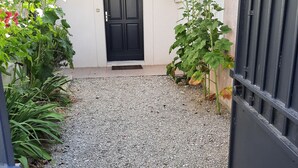 Un camino de grava que conduce a una puerta negra, con una pared blanca y un tejado de baldosas.