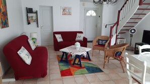 Una sala de estar con un sofá rojo, una mesita, un sillón de mimbre y una escalera.