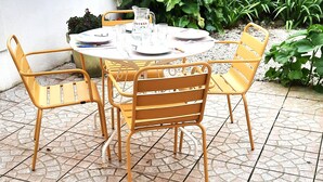 Una mesa redonda con seis sillas, una jarrón y platos dispuestos en un patio con baldosas.