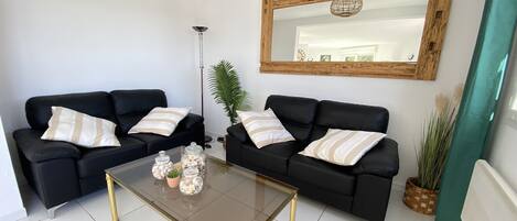 Een moderne woonkamer met twee zwarte banken, een glazen salontafel en een grote spiegel aan de muur.